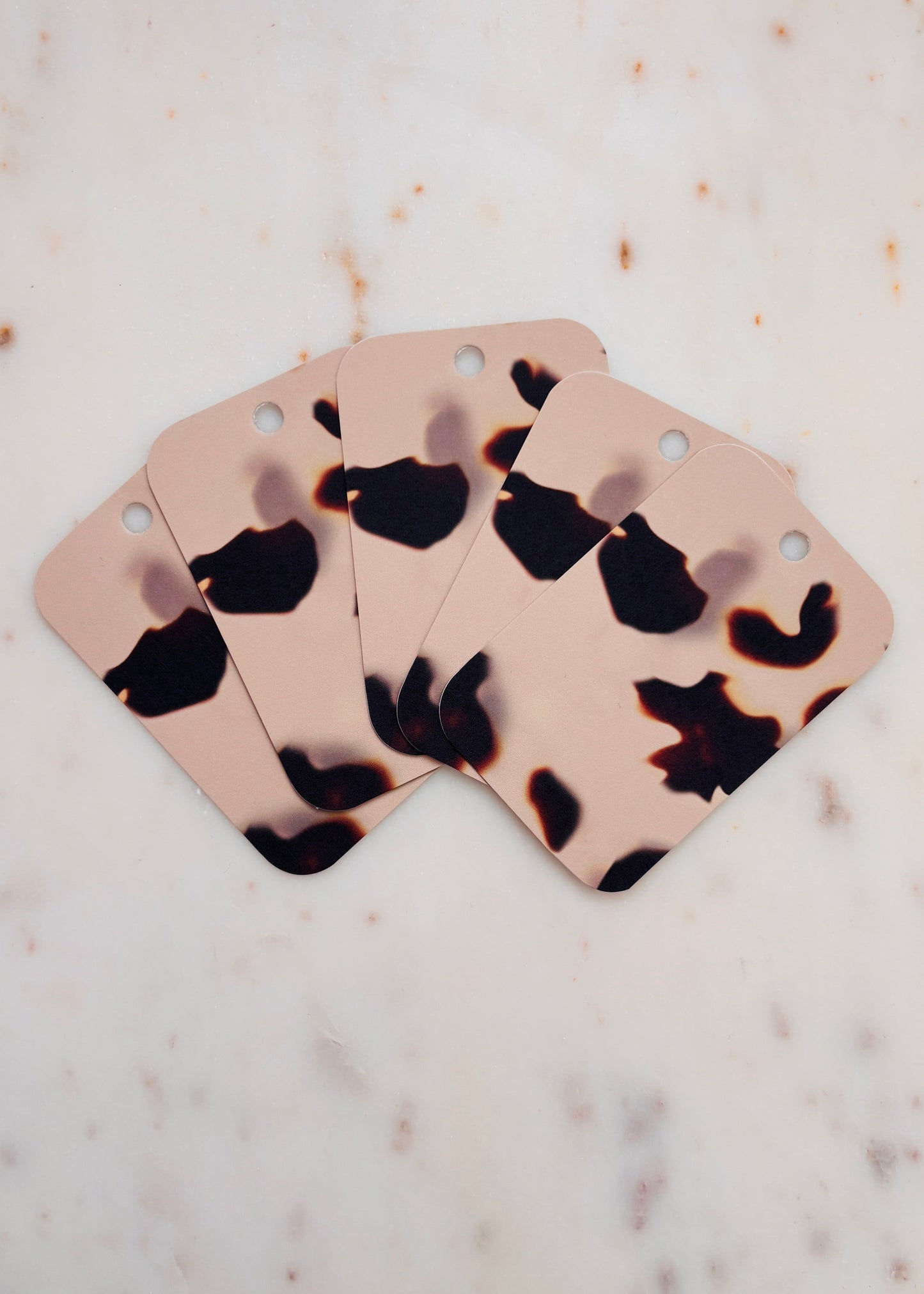 Five Tortoiseshell gift tags fanned out one on top of the other on a marble background