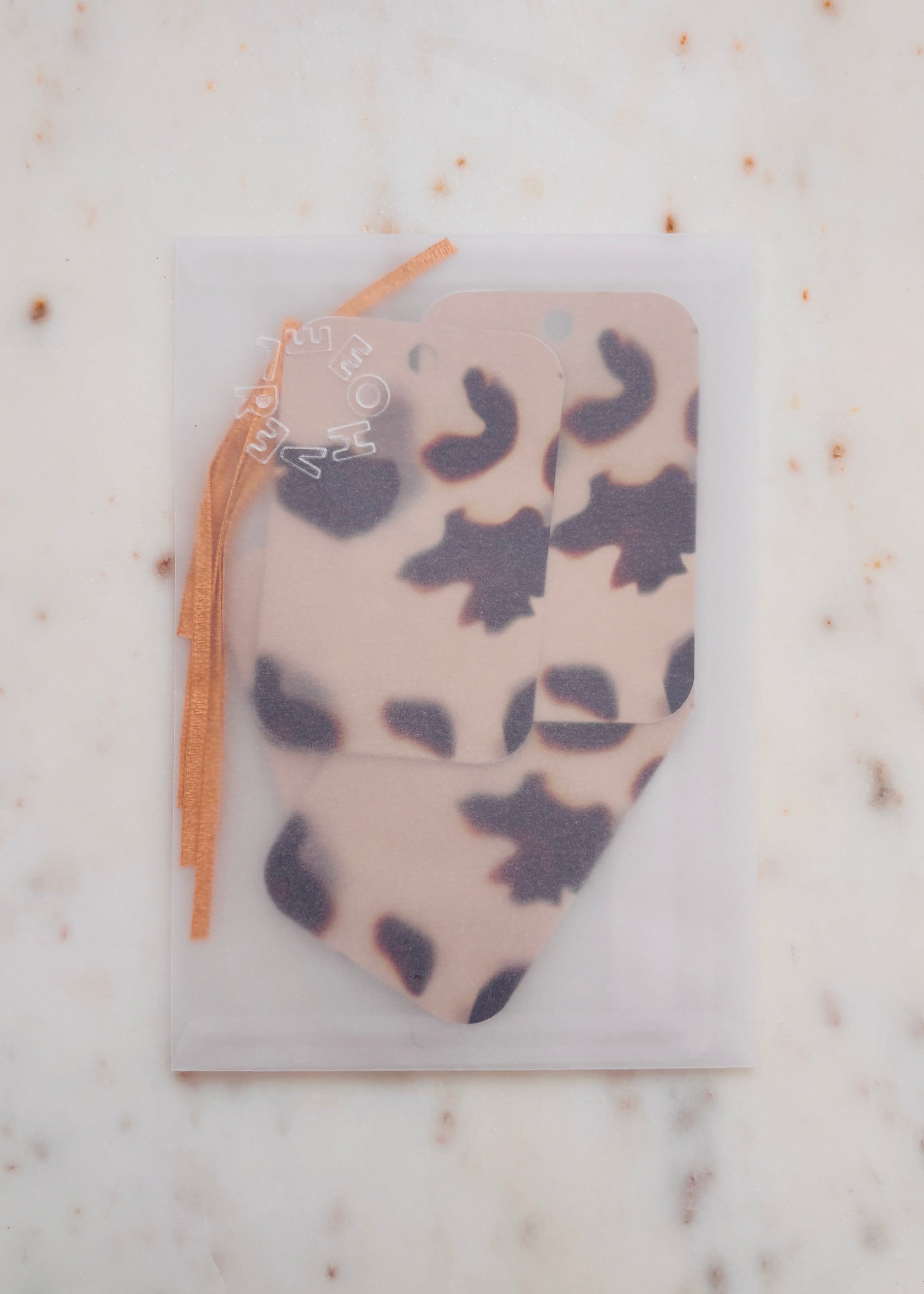Five tortoiseshell gift tags in a glassine envelope, with lame ribbon on a marble background