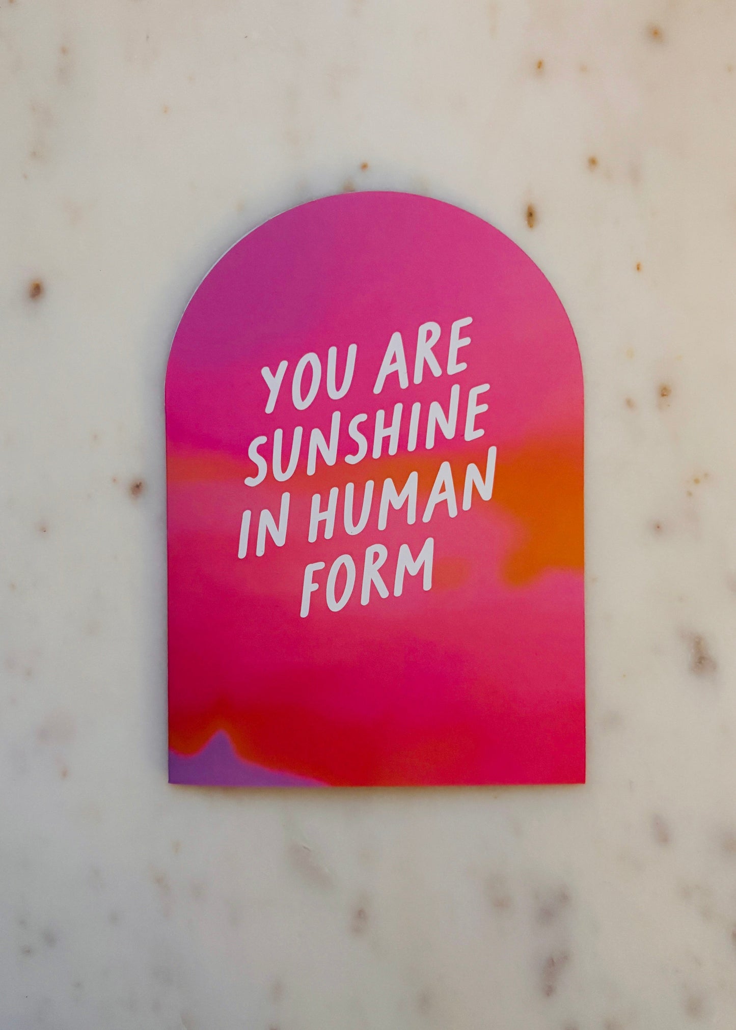 Arch shaped greeting card with 'You are sunshine in human form' text on a pink and orange gradient background. The card is on a marble background.